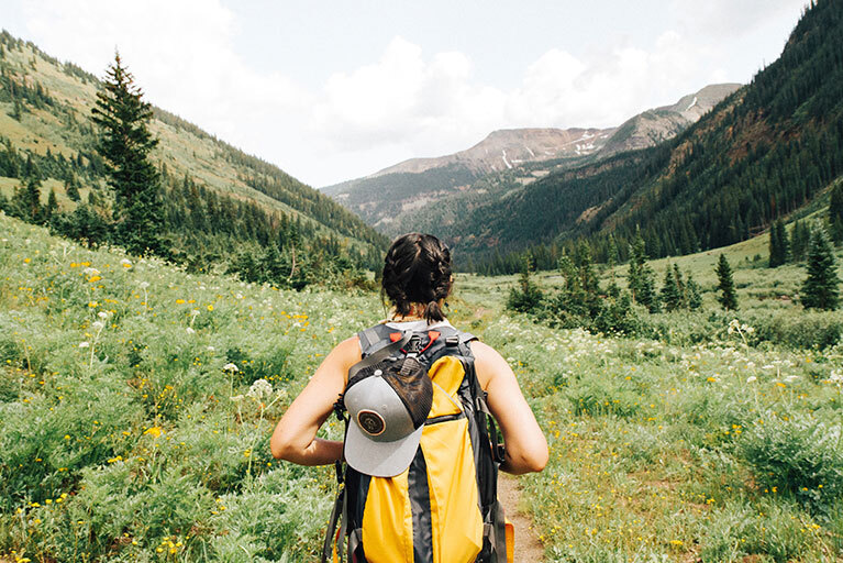 Frau steht mit Backpack auf einer Wiese und schaut in die Berge